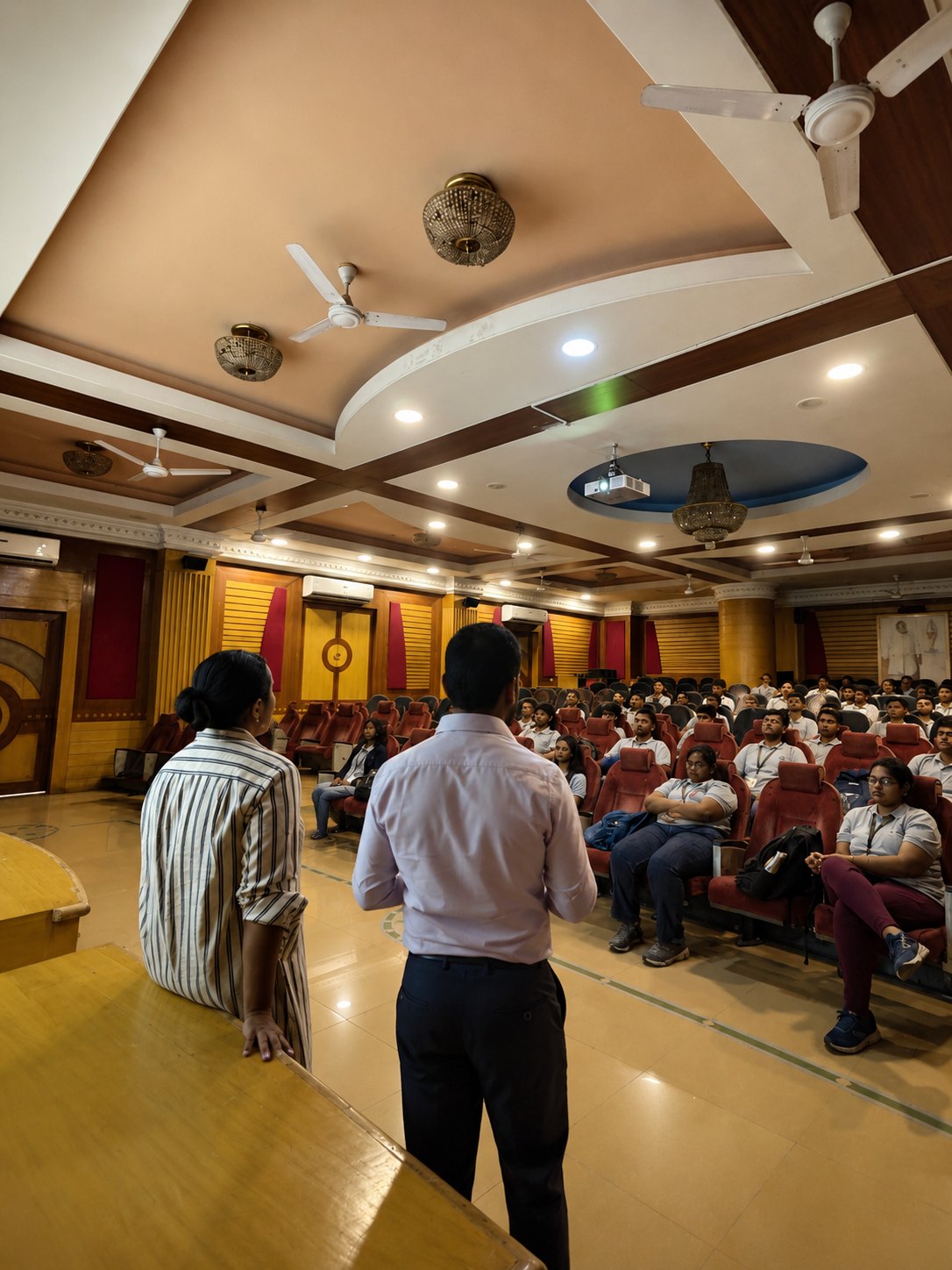 A facilitator leading a group session with students seated on the floor of the school hall