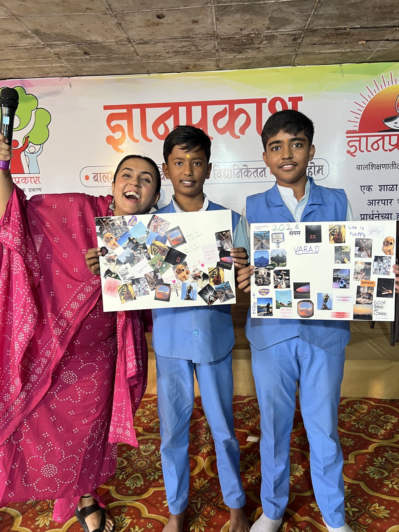 A teacher laughing with two students as they hold up their vision boards at Dnyan Prakash School