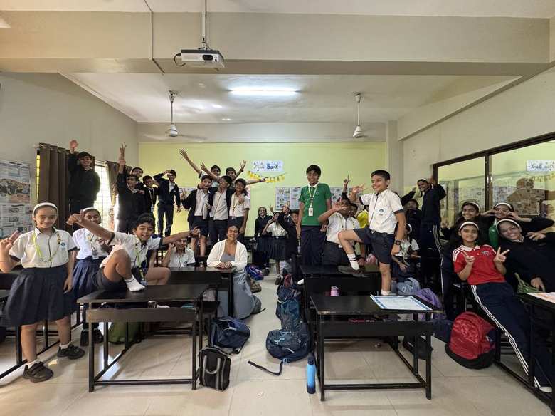 Students at GGIS standing on desks and chairs, hands raised, during an energized classroom activity